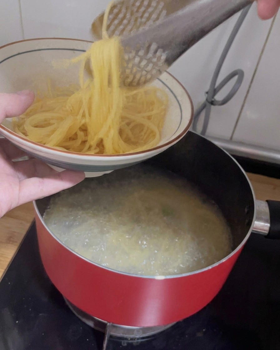 Unas pinzas levantando espaguetis cocidos de una olla hacia un bol de cerámica.