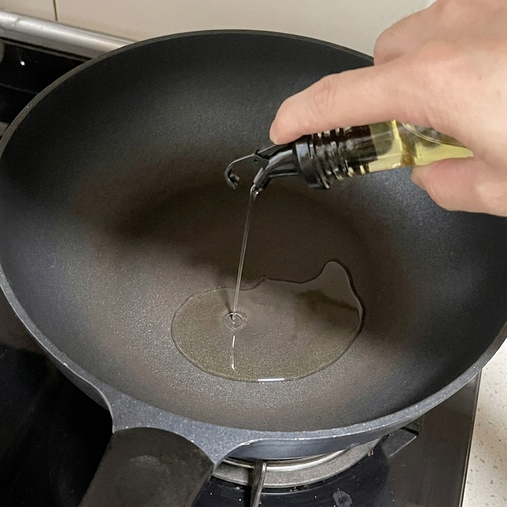 Aceite de cocina vertiéndose desde un dispensador de cristal en una sartén oscura.