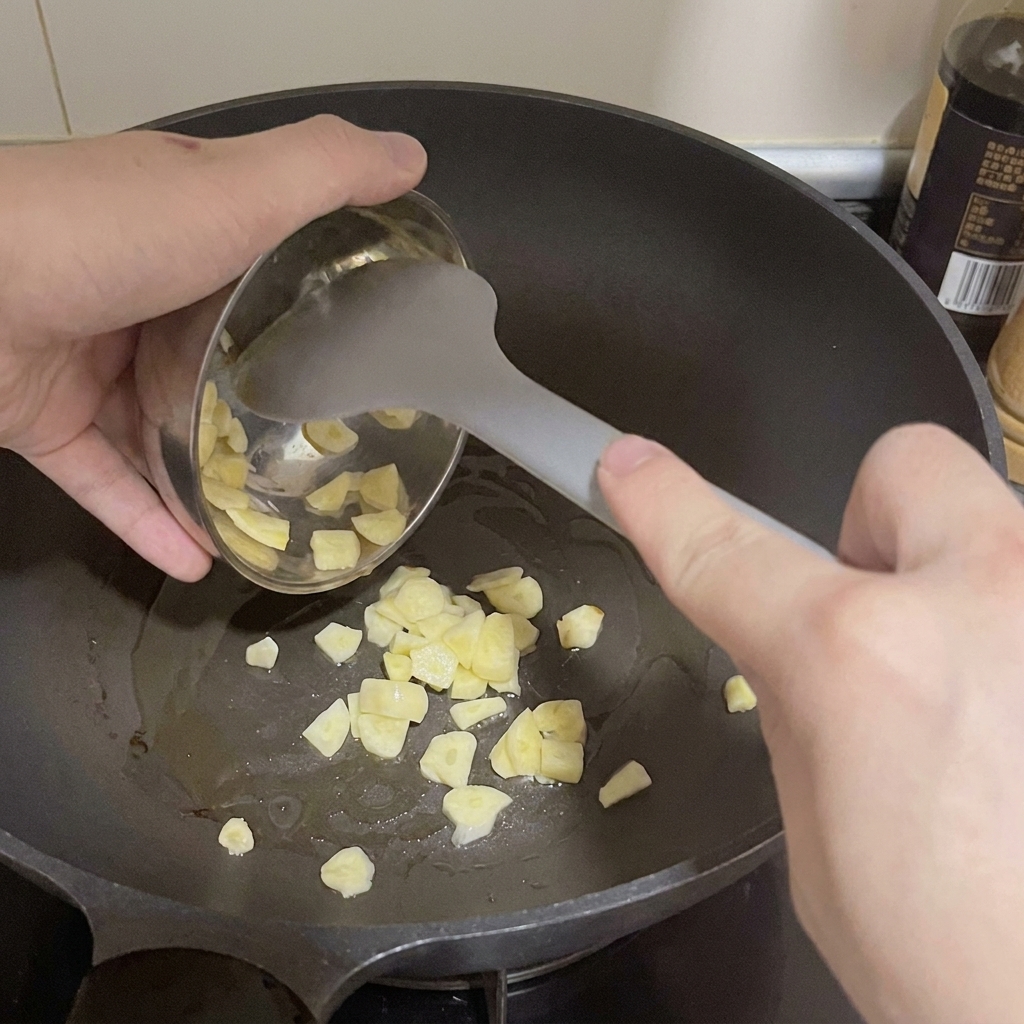 Ajo laminado pasando de un pequeño bol metálico a una sartén caliente con aceite.