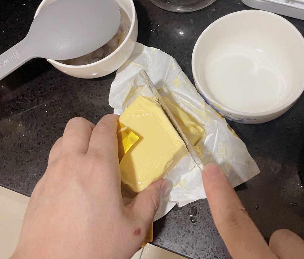 Una persona cortando una porción de un bloque de mantequilla amarilla con un cuchillo de cocina.