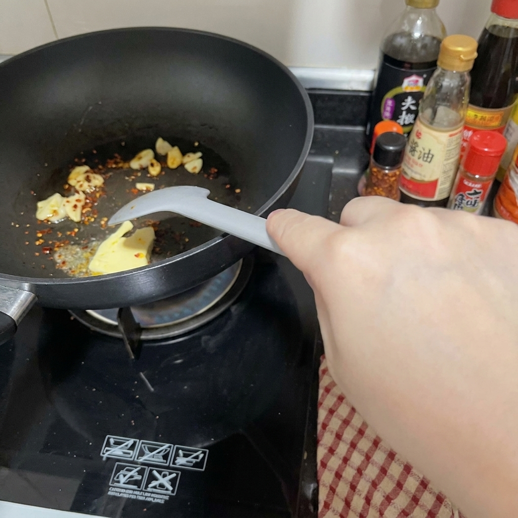 Un trozo de mantequilla derritiéndose en una sartén negra junto al ajo y el chile.