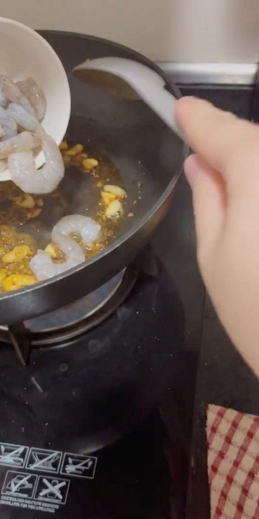 Camarones crudos y pelados vertiéndose en una sartén caliente con ajo y chile.