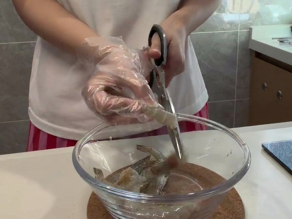 Una persona con guantes utiliza tijeras para limpiar con cuidado el lomo de una gamba cruda.
