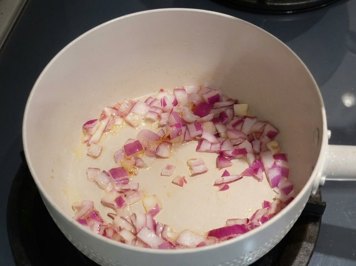 Cebolla morada picada siendo sofrita en aceite en una sartén de color claro.
