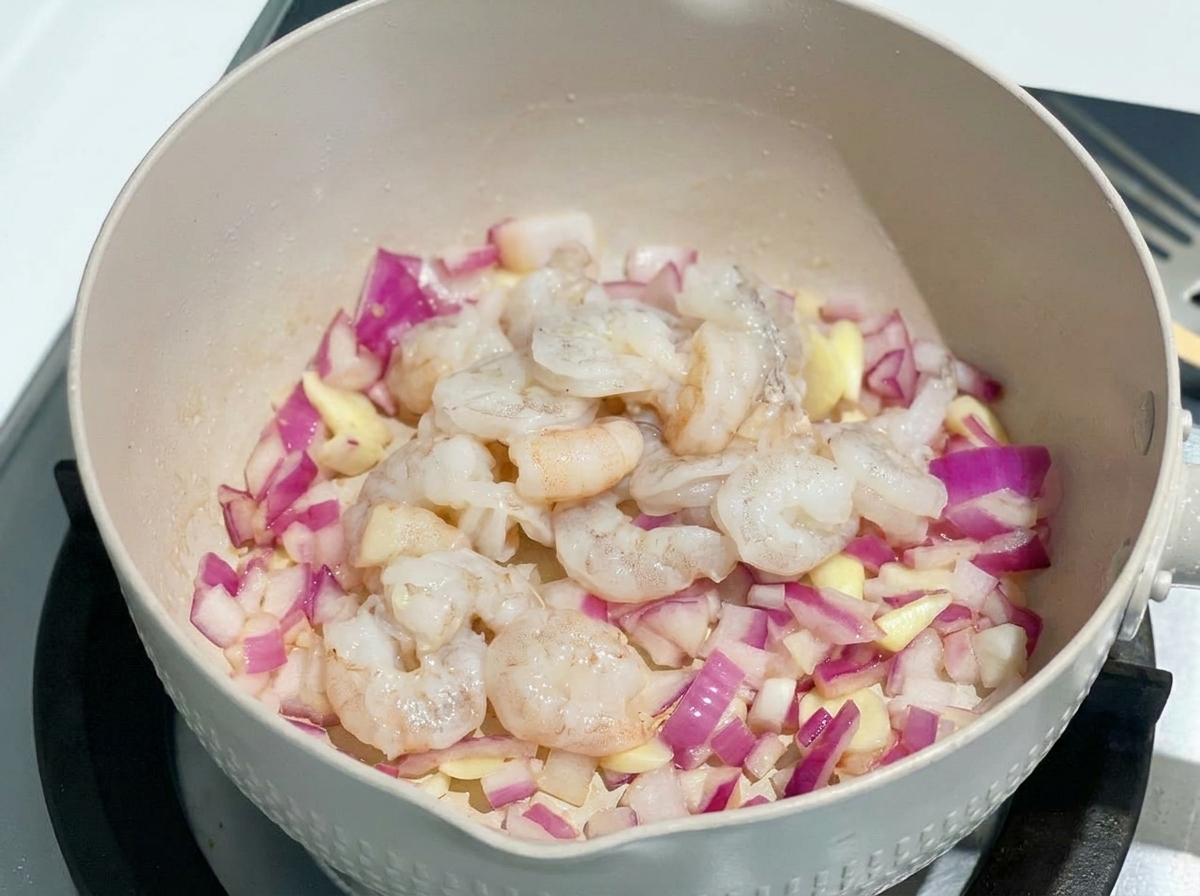 Camarones crudos añadidos a la sartén con la cebolla morada sofrita.