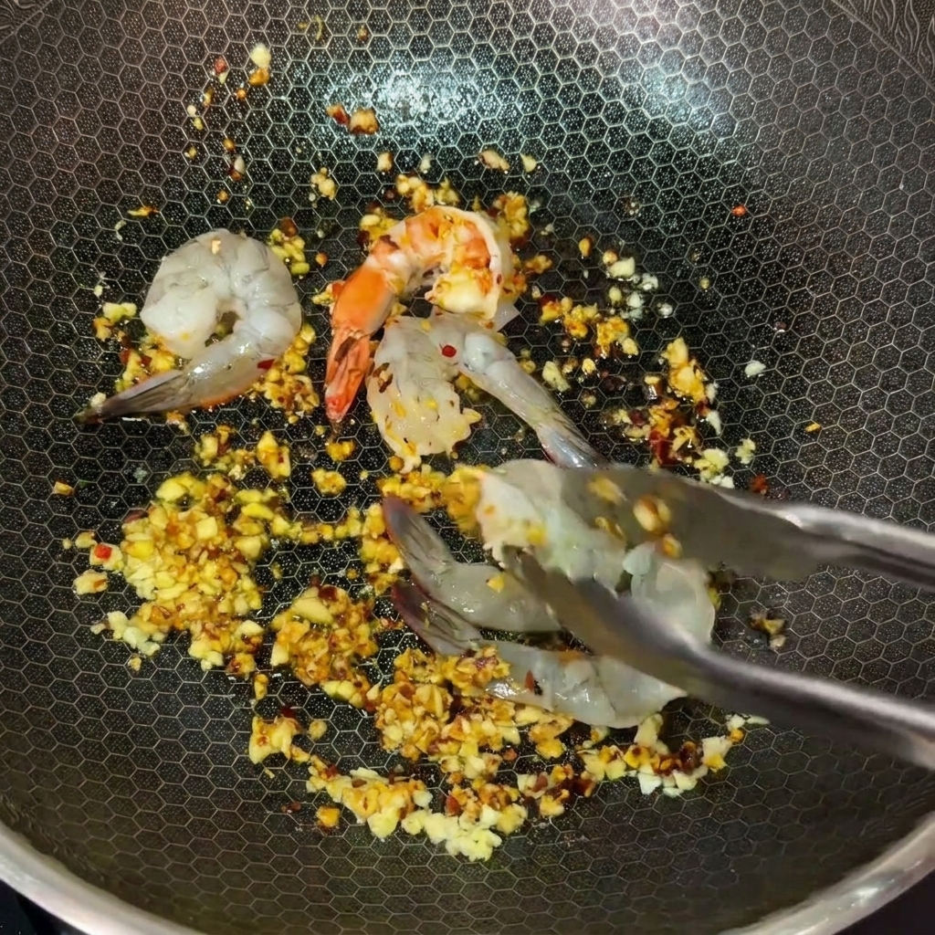 Usando pinzas de metal para colocar camarones crudos en un wok caliente lleno de mantequilla con ajo y chile.
