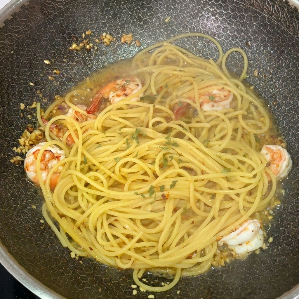 Espaguetis y camarones en un wok caliente siendo decorados con perejil verde recién picado.