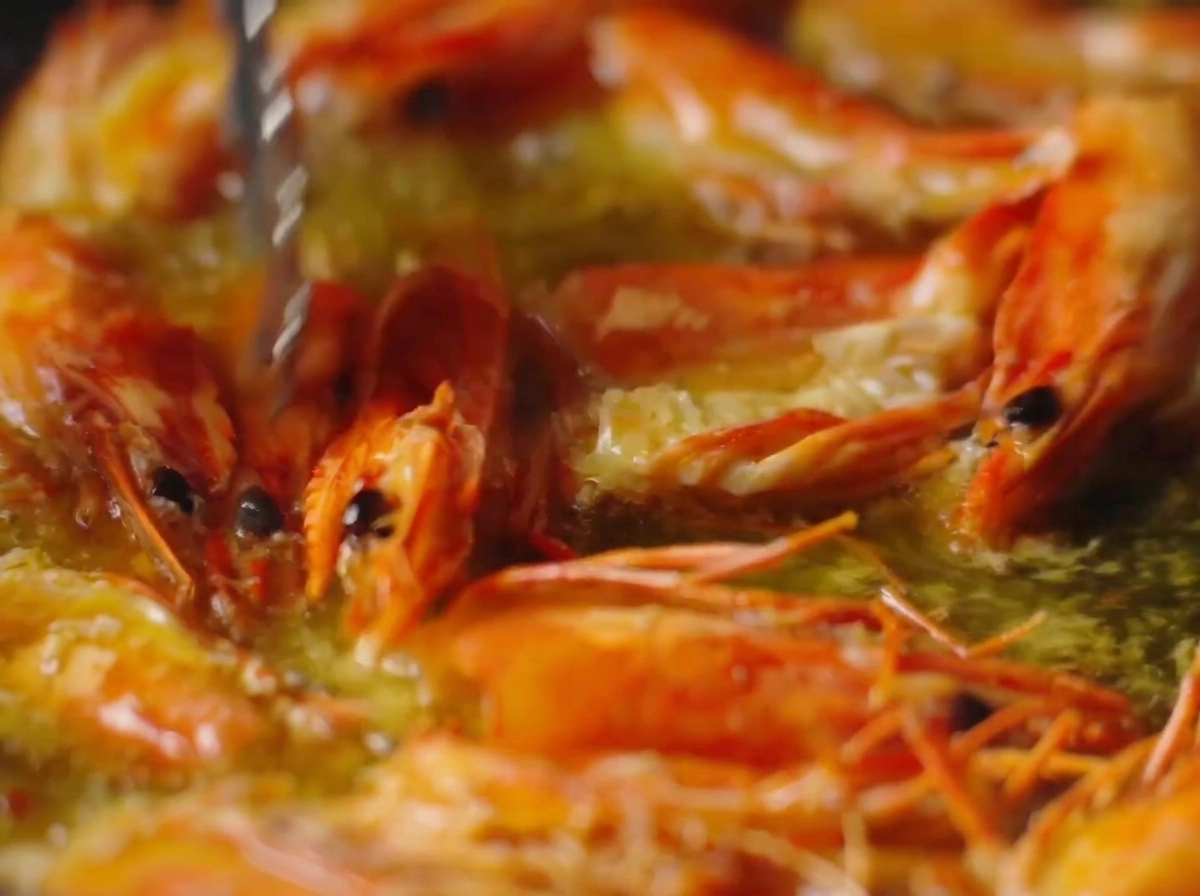 Pinzas presionando cabezas de gambas de color naranja vibrante en aceite burbujeante.