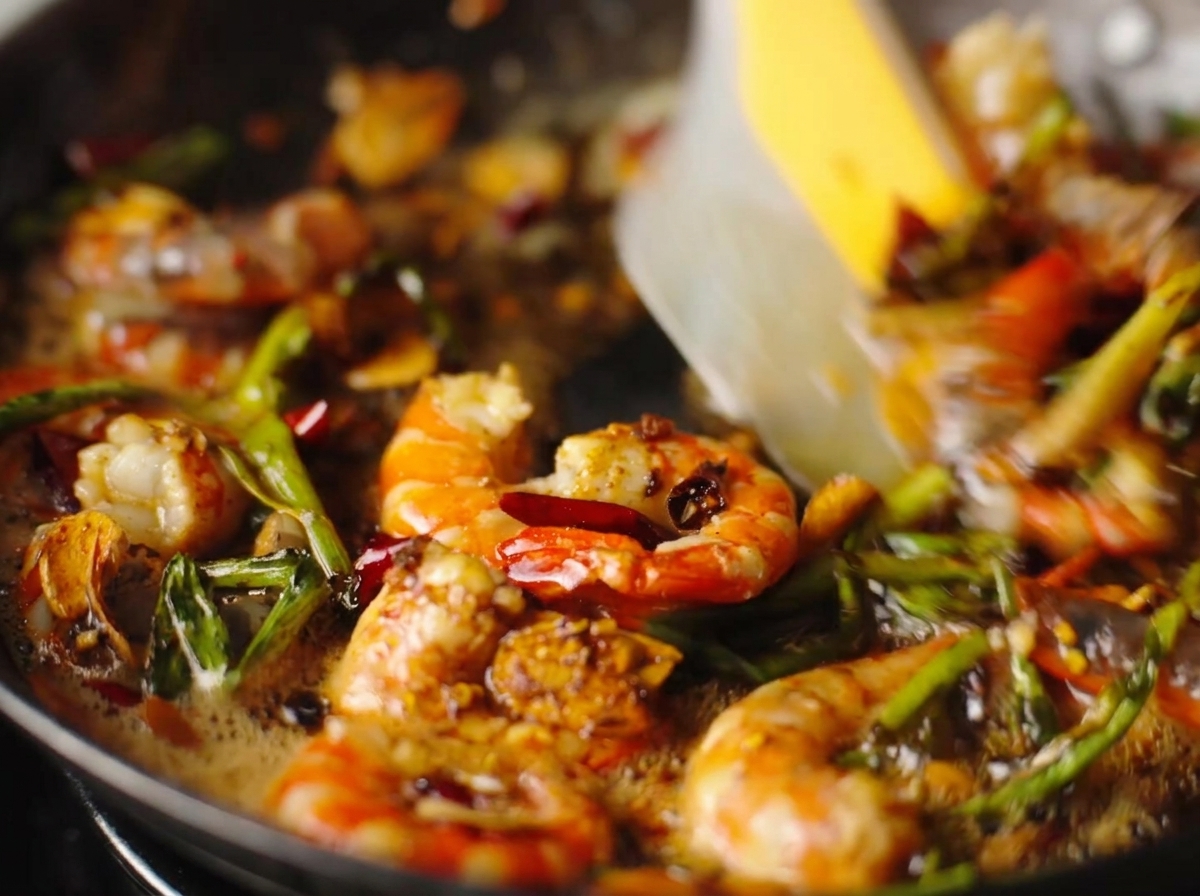 Gambas peladas salteándose con ajo, chiles y cebolletas en una sartén caliente.