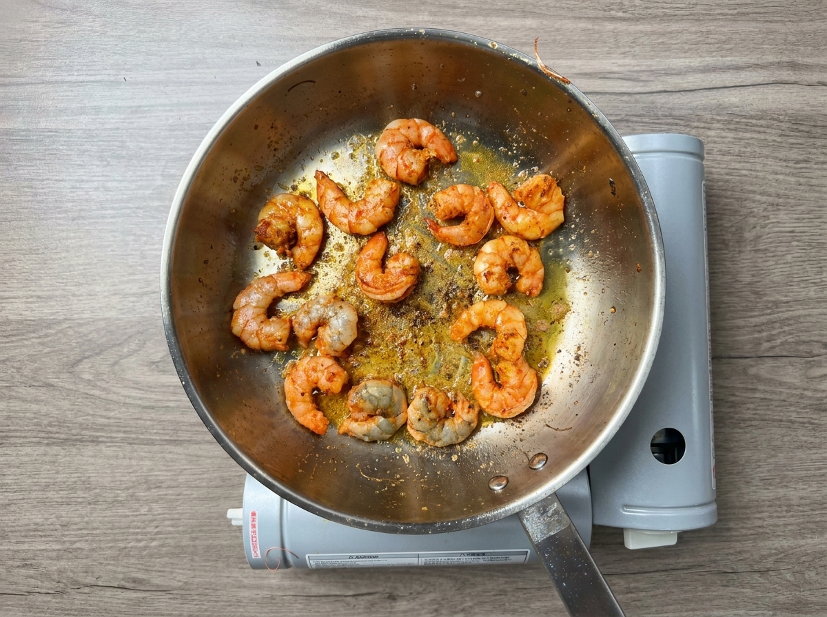 Camarones pelados y sazonados cocinándose en aceite rojizo infusionado.