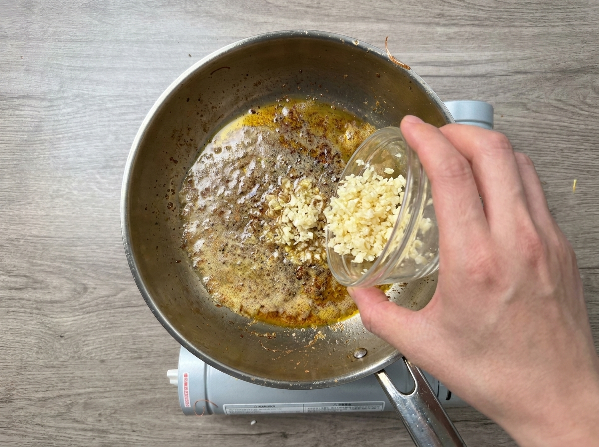 Ajo picado vertiéndose en una sartén caliente con mantequilla derretida y aceite.