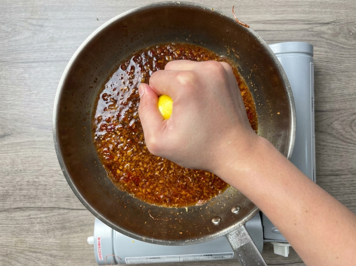 Una mano exprimiendo medio limón sobre una salsa de ajo burbujeante.