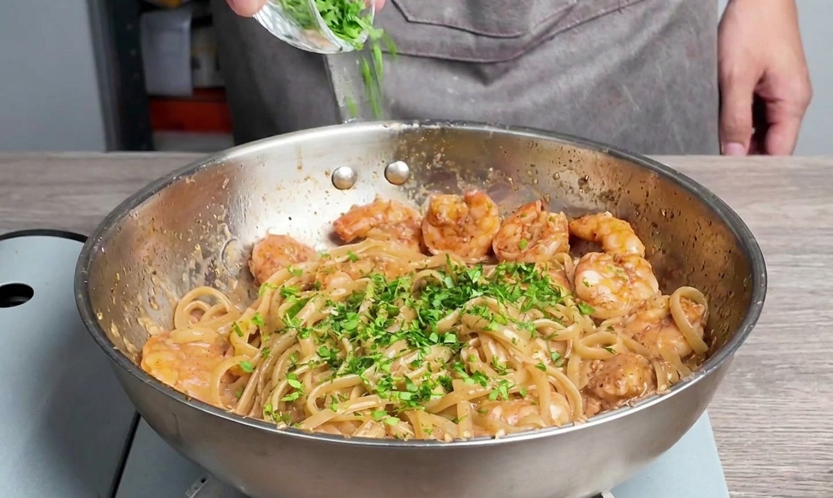 Perejil fresco picado espolvoreado sobre linguine y camarones en la sartén.