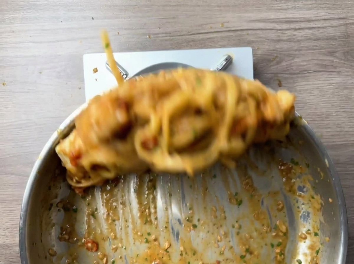 Pasta y camarones mezclándose vigorosamente en la sartén.