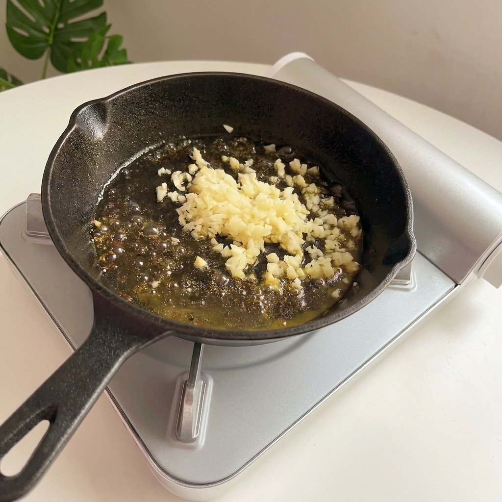 Ajo picado burbujeando y dorándose en mantequilla derretida dentro de una sartén de hierro.