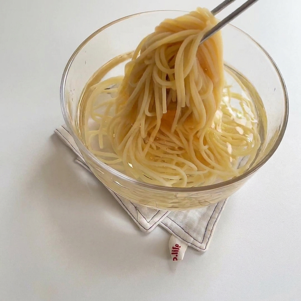 Espaguetis cocidos introduciéndose en un bol de cristal con agua fría.
