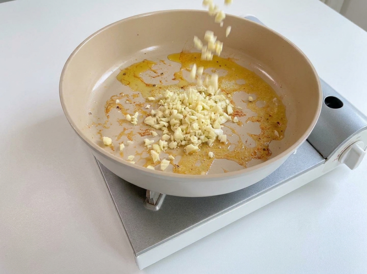 Ajo picado cayendo en una sartén caliente con restos de aceite y mantequilla.