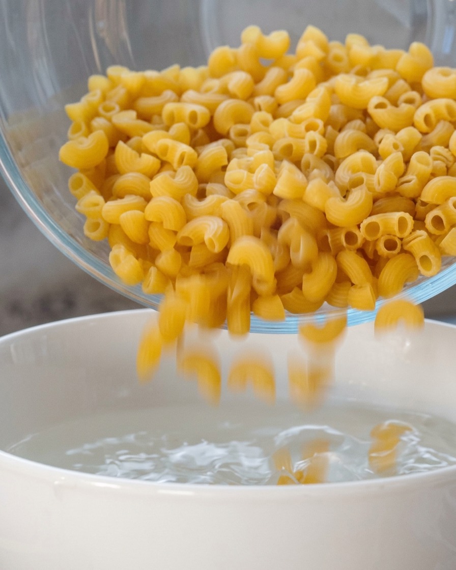 Macarrones secos en espiral vertiéndose en una olla blanca con agua caliente.