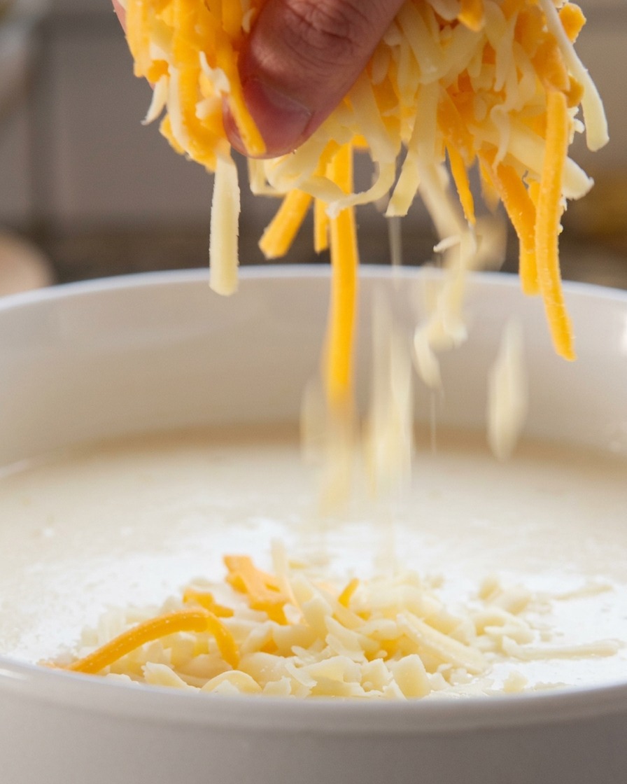 Esparciendo una mezcla de queso blanco y naranja rallado en un líquido caliente dentro de una olla.