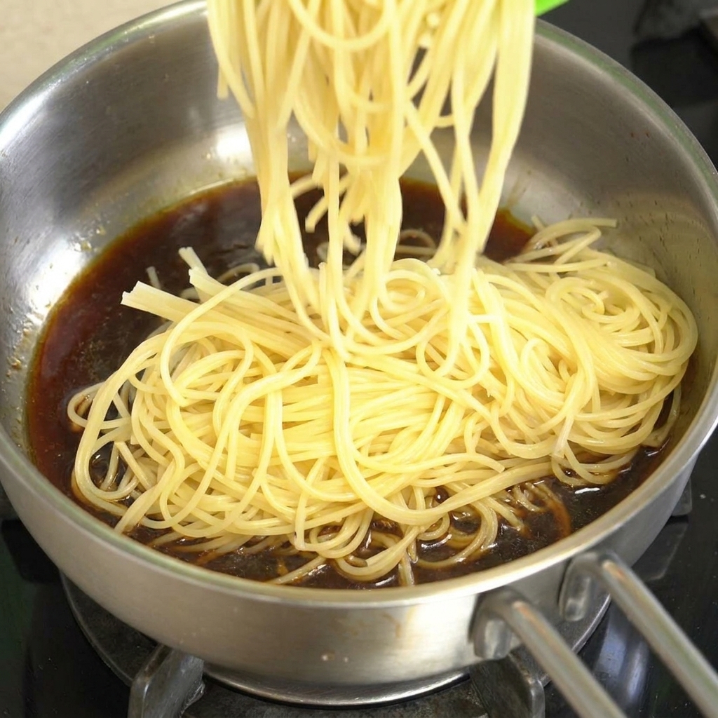 Espaguetis cocidos siendo añadidos a una sartén con salsa de ternera a la pimienta negra.