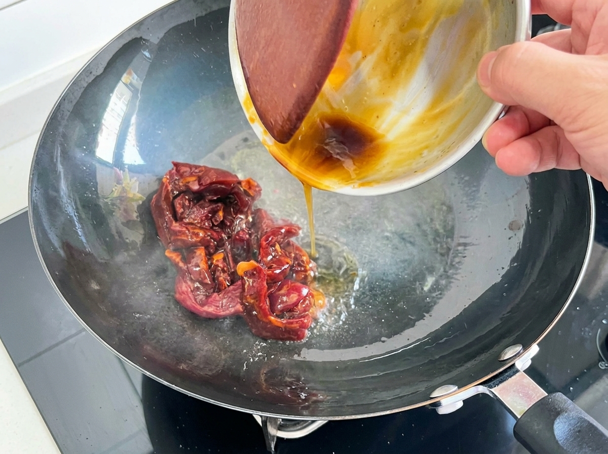 Tiras de carne roja marinada salteándose en un wok caliente con aceite.
