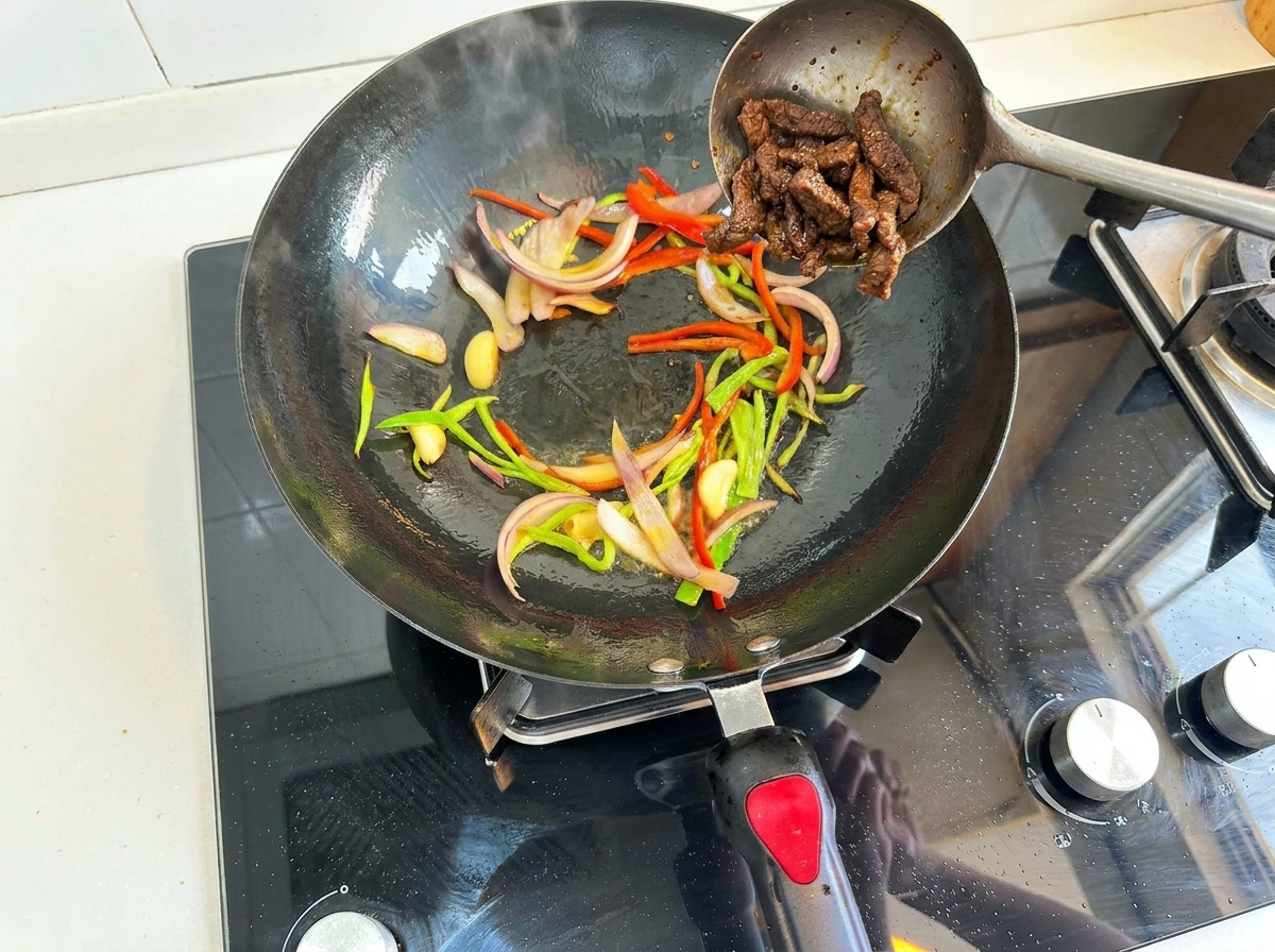 Tiras de ternera precocinadas volviendo al wok con pimientos, cebolla y ajo salteados.