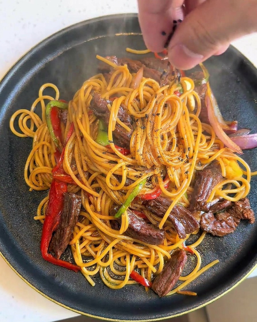 Mano espolvoreando semillas de sésamo negro sobre un plato de espaguetis con ternera recién hecho.