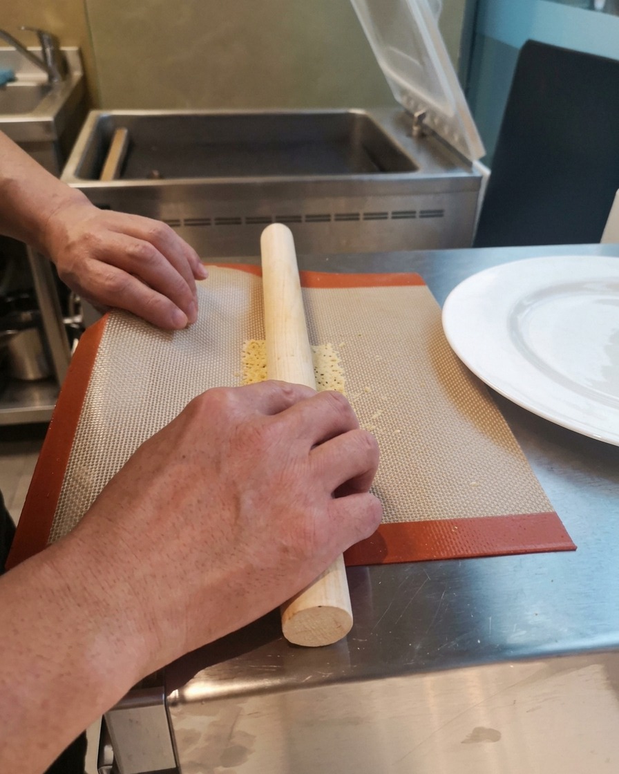 Manos envolviendo con cuidado un crujiente horneado caliente y flexible alrededor de un rodillo de madera sobre un tapete de silicona.