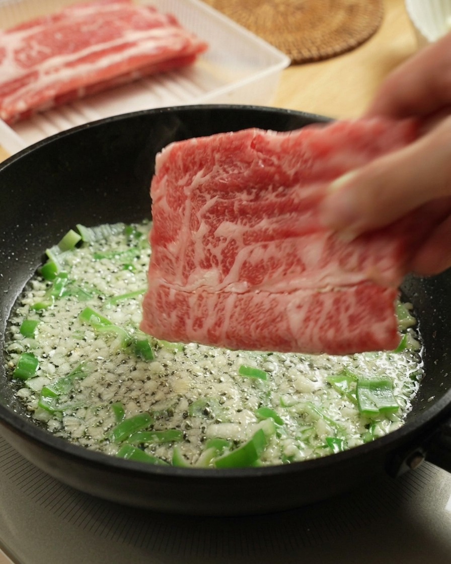 Colocando láminas de ternera cruda en una sartén caliente con cebolleta y ajo salteados.