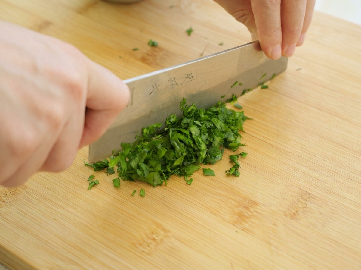 Manos picando finamente hojas de perejil verde fresco con un cuchillo de cocina sobre una tabla de madera.