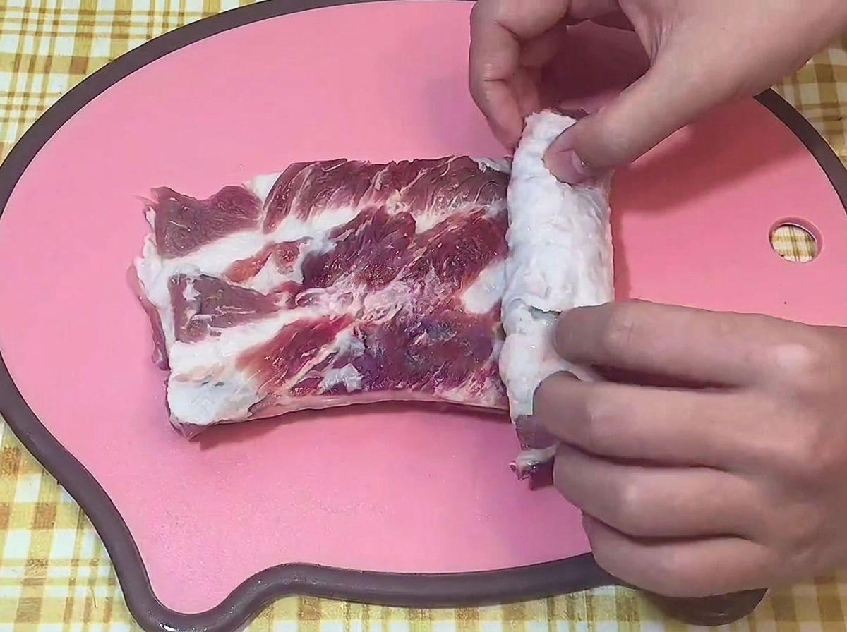 Manos enrollando la panceta cruda para formar un cilindro apretado sobre una tabla de cortar.