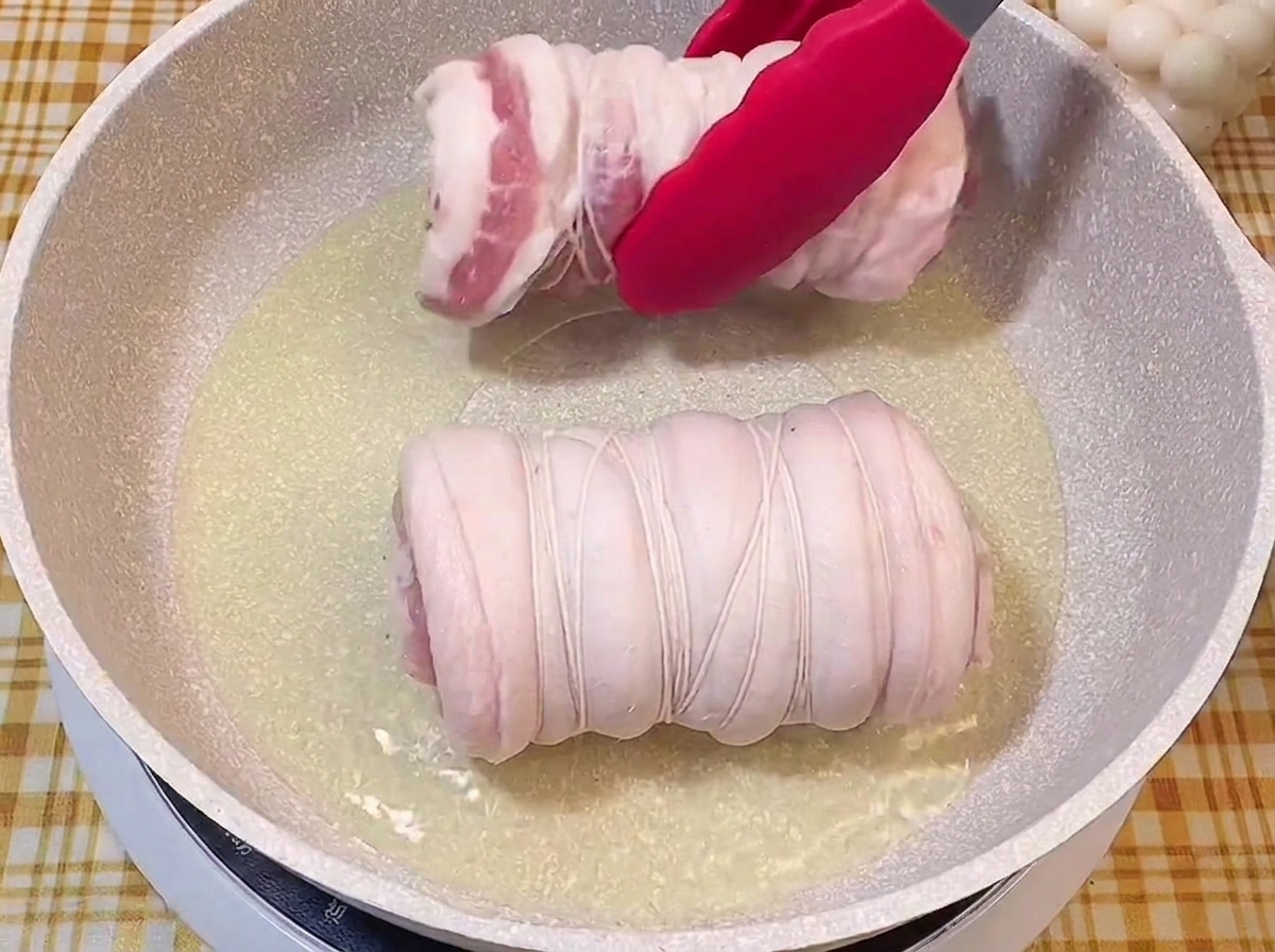 Pinzas rojas colocando los rollos de cerdo en una sartén con aceite caliente.