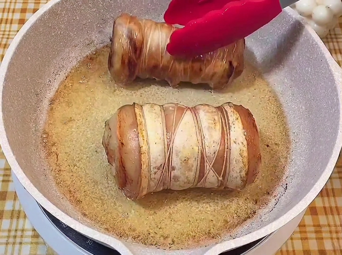Dos rollos de cerdo con un exterior dorado y crujiente burbujeando en la sartén.