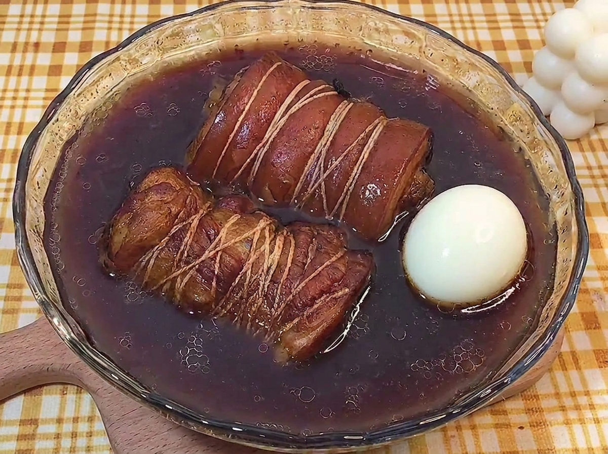 Dos rollos de chashu y un huevo cocido reposando en un bol con el líquido del braseado.