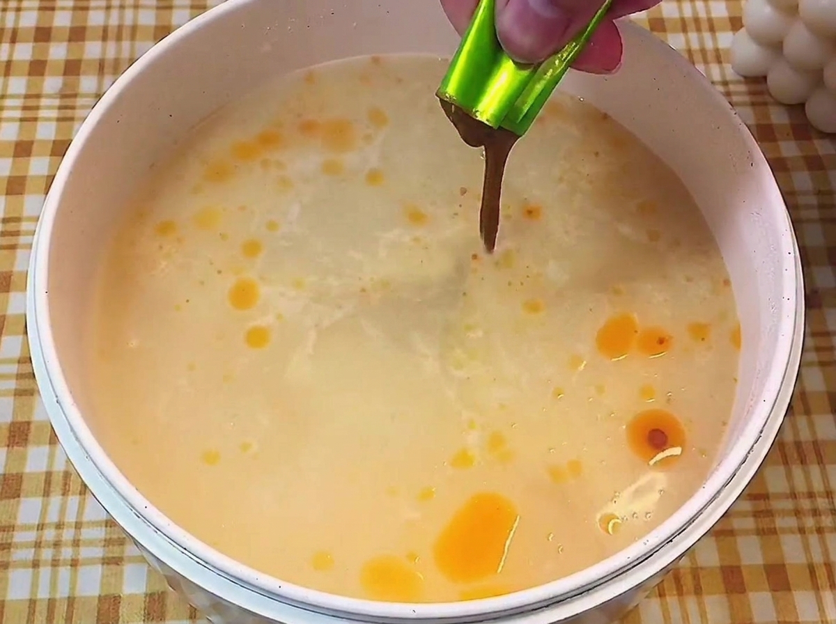 Mano vertiendo el sobre de base líquida concentrada en una olla con caldo claro hirviendo.