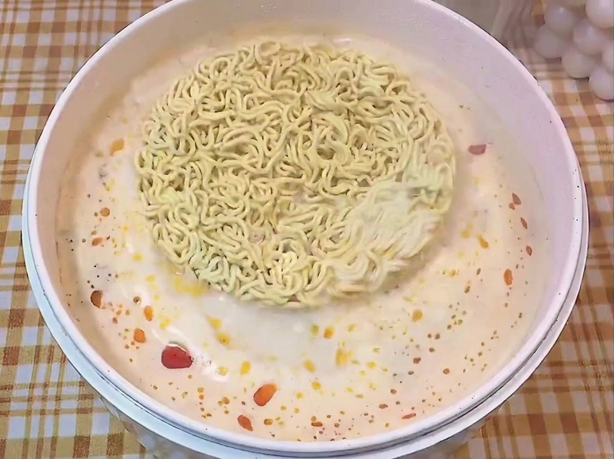Bloque de fideos secos flotando en una olla blanca con caldo sazonado hirviendo.
