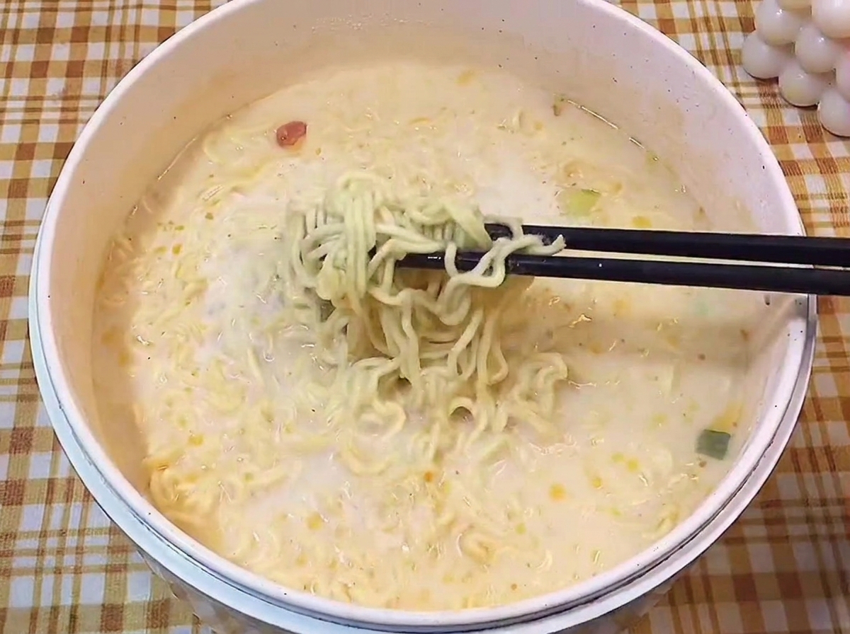 Palillos negros levantando fideos ondulados de un caldo cremoso.