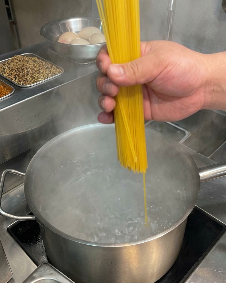 Una mano poniendo espaguetis secos en una olla de agua hirviendo.