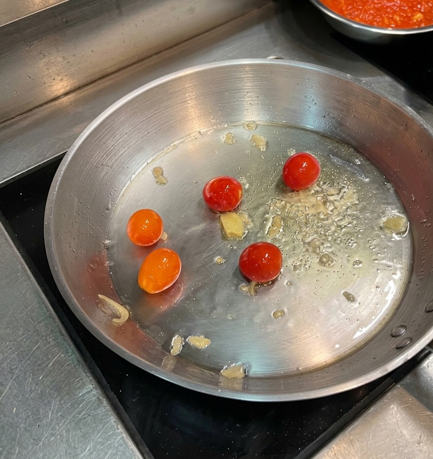 Tomates cherry dorándose en aceite caliente en una sartén de acero inoxidable.