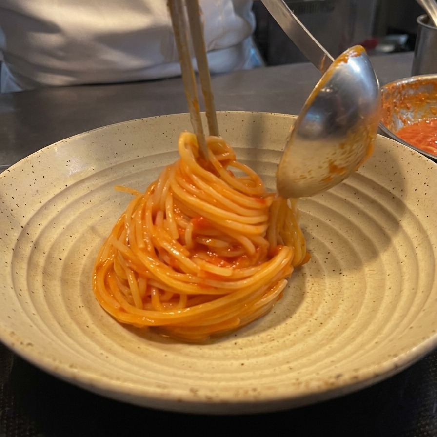 Un chef usando pinzas y un cazo para enrollar los espaguetis en un nido sobre un plato cerámico.
