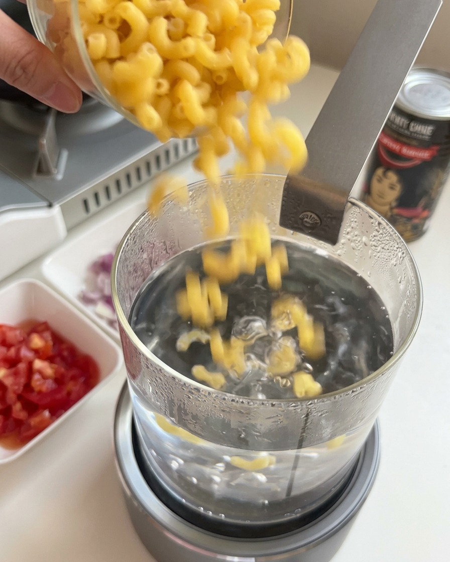 Vertiendo coditos de pasta seca en una olla de vidrio con agua hirviendo.