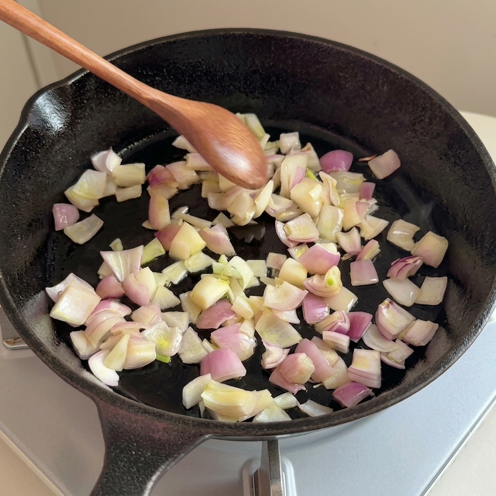 Cebolla picada sofriéndose en una sartén de hierro con una cuchara de madera.
