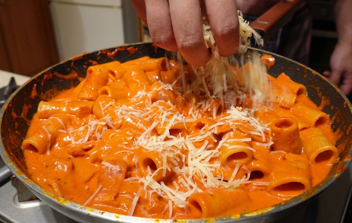 Queso parmesano rallado espolvoreado a mano sobre rigatoni mezclado con salsa rosa.