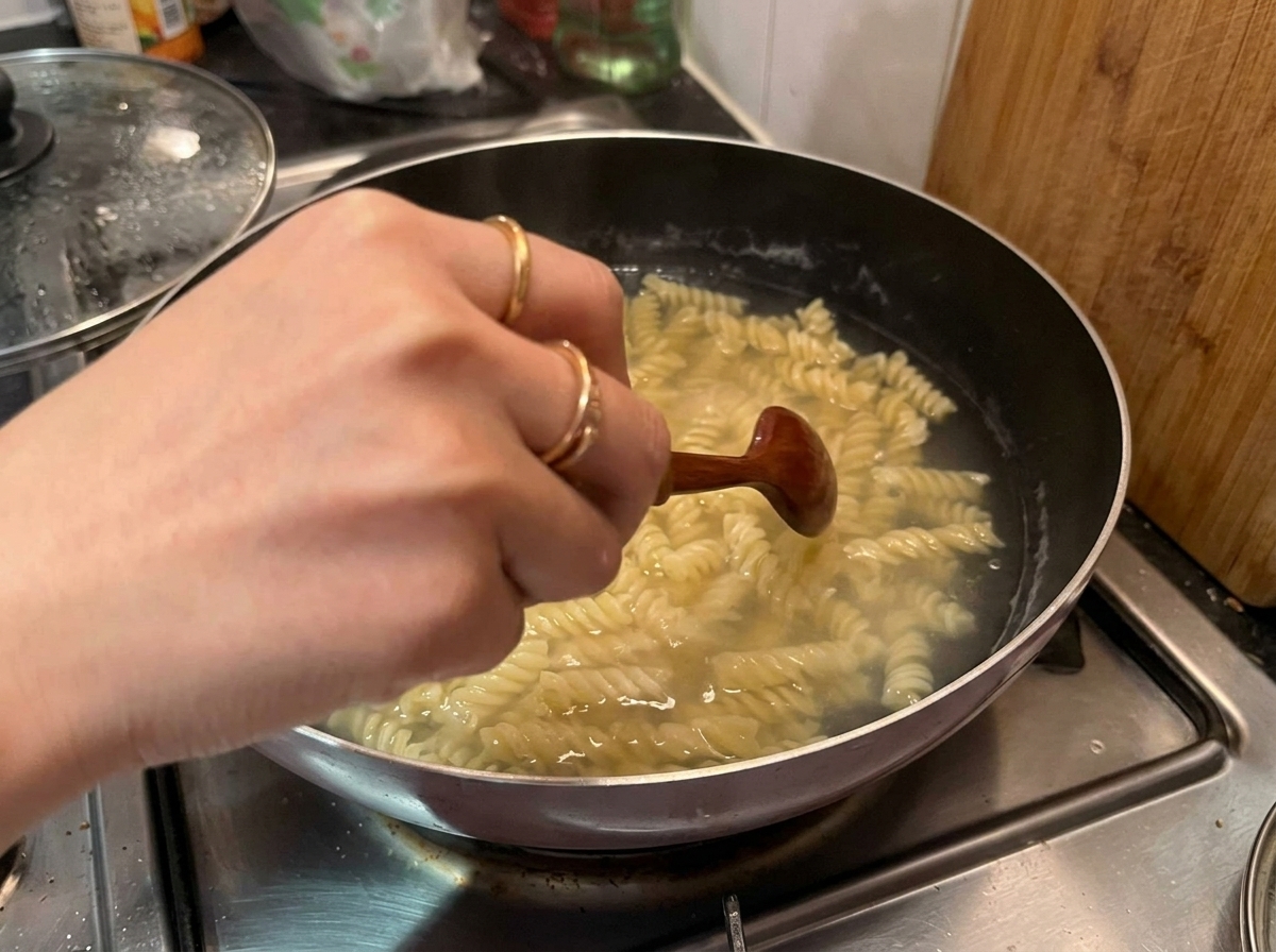 Una mano usando una cuchara de madera para remover y sacar los fusilli cocidos de una olla con agua hirviendo.