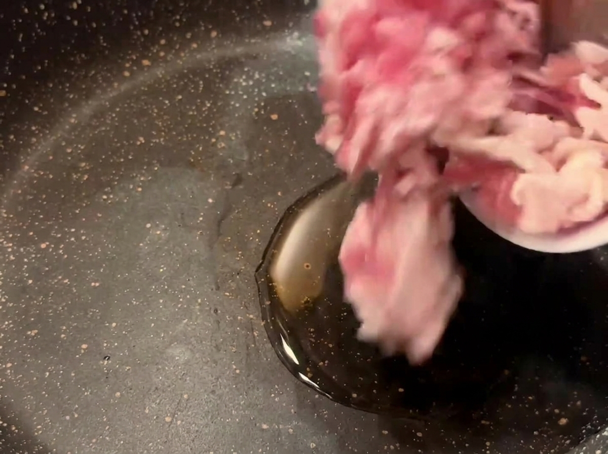 Trozos de beicon crudo cayendo desde un cuenco pequeño a una sartén oscura con aceite de cocina caliente.