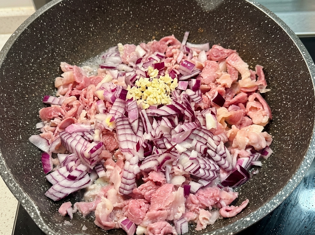 Un pequeño montón de ajo fresco picado sobre cebolla roja salteada y beicon en una sartén de cocina.