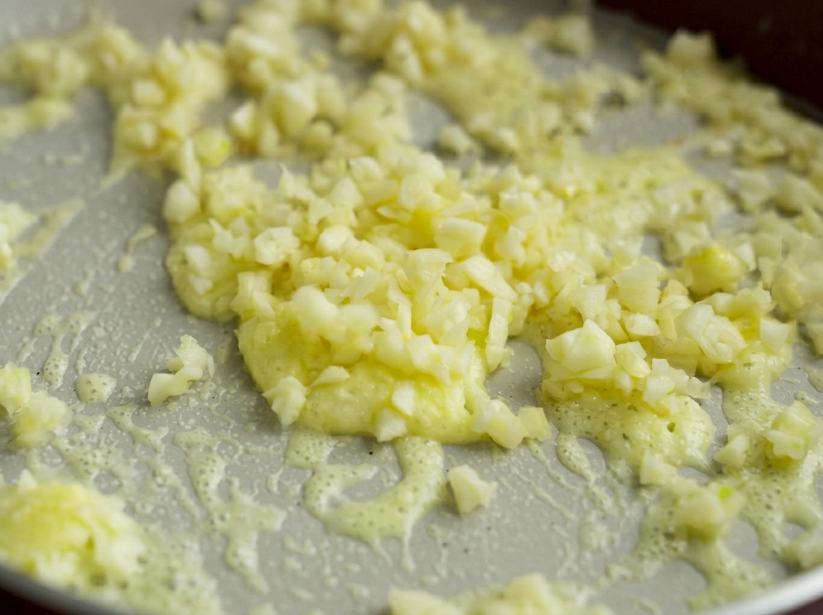 Trocitos de ajo finamente picados cocinándose suavemente en una base burbujeante de mantequilla derretida y maicena.