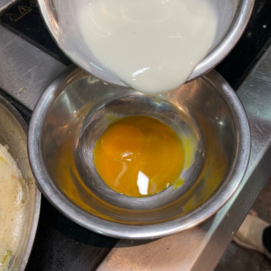 Nata líquida vertiéndose en un pequeño cuenco que contiene una yema de huevo naranja vibrante.