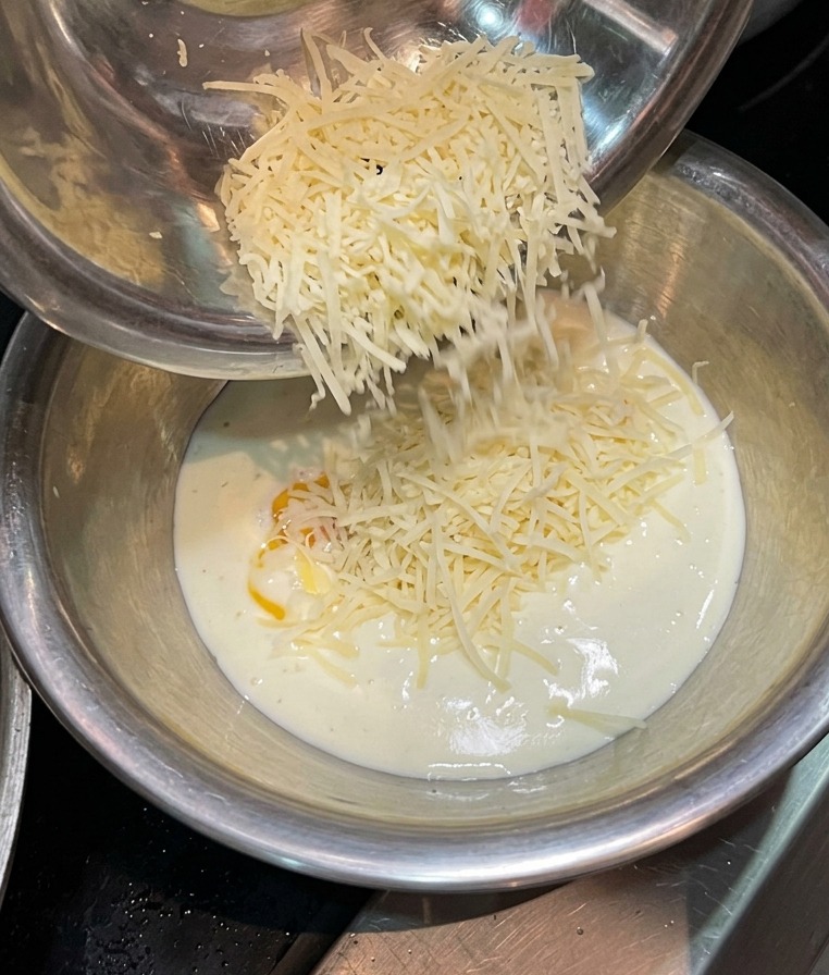 Queso rallado cayendo desde un cuenco metálico en una mezcla de nata y yema de huevo.