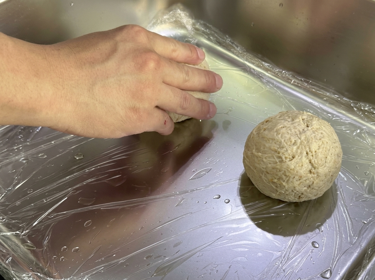 Bolas de masa con forma colocadas en una bandeja de metal cubierta con papel film transparente para su fermentación.